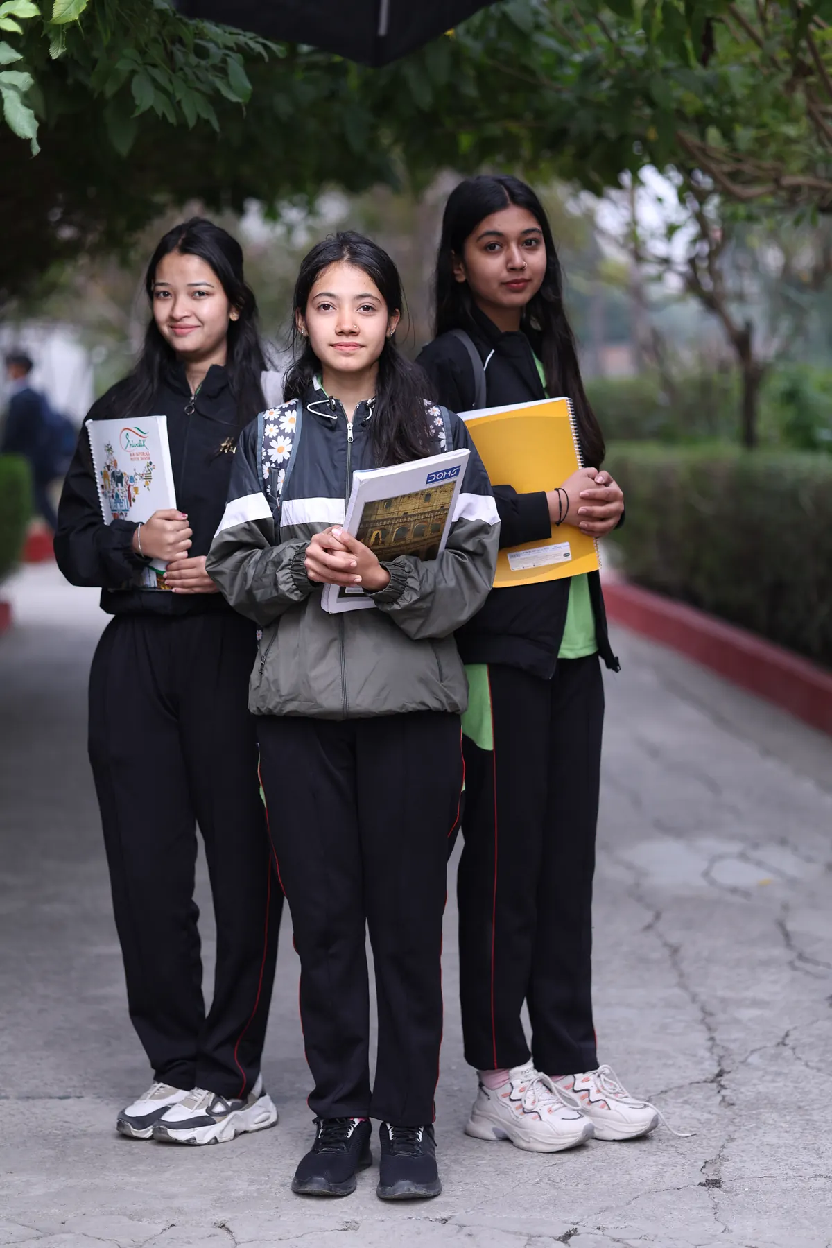 Three students holding books on a campus pathway